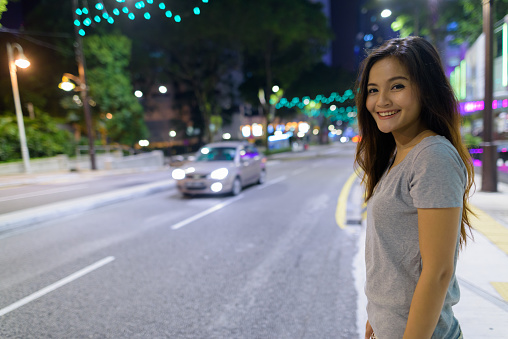 Portrait of young beautiful Asian woman wandering in the city streets at night in Kuala Lumpur, Malaysia horizontal shot