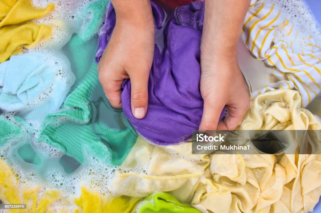 Female hands wash colored clothes in basin. Clothing Stock Photo