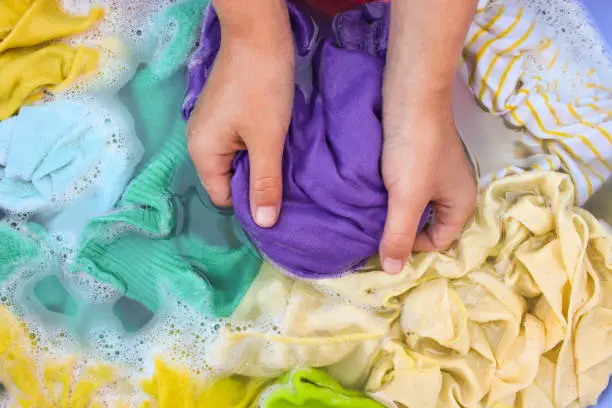 Photo of Female hands wash colored clothes in basin.