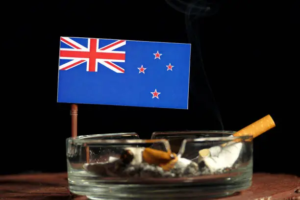 New Zealand flag with burning cigarette in ashtray isolated on black background