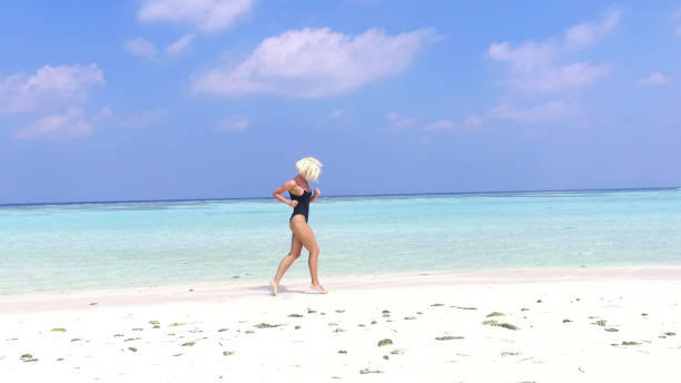 mujer en bikini corriendo por el agua en playa, maldivas - blond hair overcast sun sky fotografías e imágenes de stock