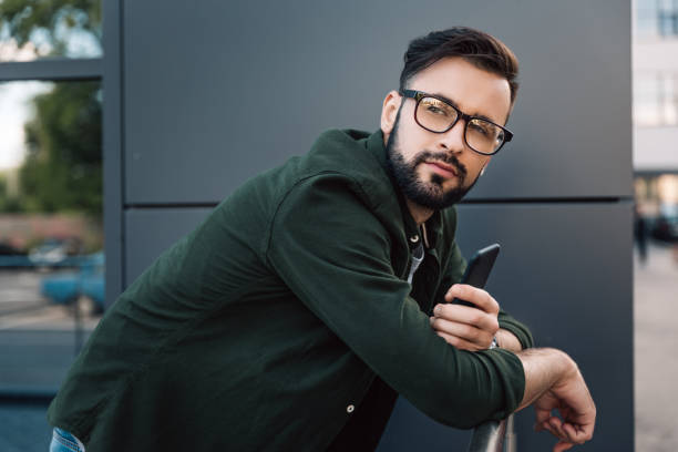 istock pensive bearded young man in eyeglasses holding smartphone 807281692