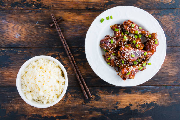 Crispy sesame chicken wings with a sticky sweet Asian sauce and white boiled rice on a plate on wooden table, top view. Crispy sesame chicken wings with a sticky sweet Asian sauce and white boiled rice on a plate on wooden table, top view. sticky sesame chicken sauces stock pictures, royalty-free photos & images