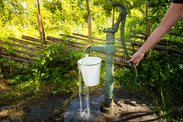 Old retro hand water pump outside in the garden. A hand is pumping and you can see the motion.