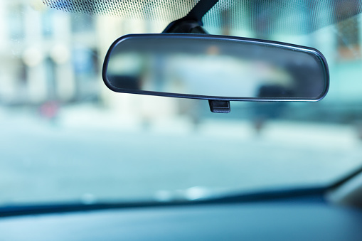 Helpful equipment. The close up of a black-rimmed rear-view mirror being adjusted to the clean windshield of a car