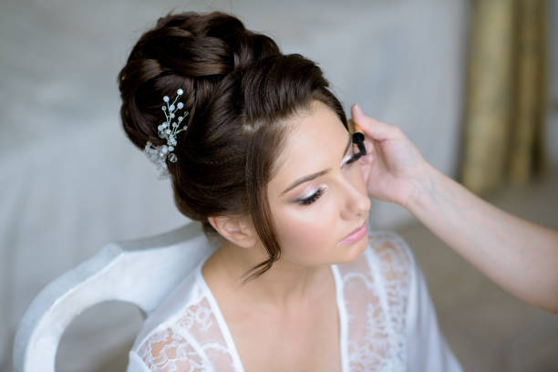 Wedding makeup artist making a make up for bride. Beautiful sexy model girl indoors. Beauty woman with curly hair. Female portrait. Bridal morning of a cute lady. Close-up hands near face