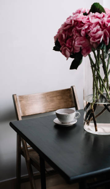 istock Huge, beautiful and fluffy pink hydrangea on the black wooden coffee table with a coffee cup (filled with pink ranunculus instead of coffee), with a wooden chair on the background. 807332368