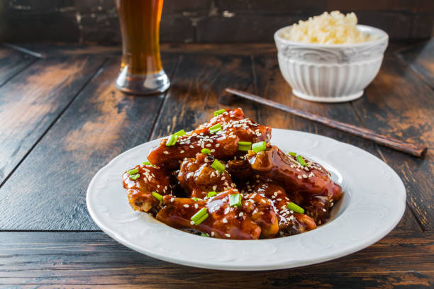 Crispy sesame chicken wings with a sticky sweet Asian sauce and white boiled rice on a plate on wooden table. Crispy sesame chicken wings with a sticky sweet Asian sauce and white boiled rice on a plate on wooden table. sticky sesame chicken sauces stock pictures, royalty-free photos & images