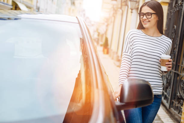 Pretty woman with coffee cup touching her car