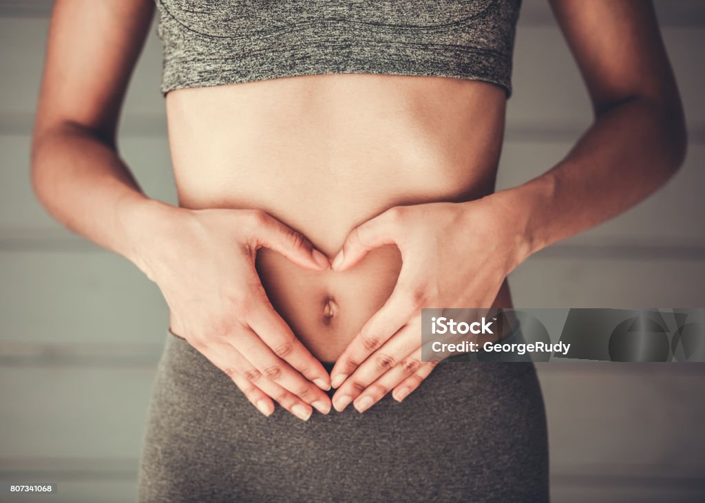 Afro American girl doing sport Cropped image of slim Afro American girl in sportswear showing heart on her stomach Abdomen Stock Photo