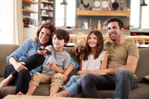 istock Family Sitting On Sofa In Open Plan Lounge Watching Television 807350044