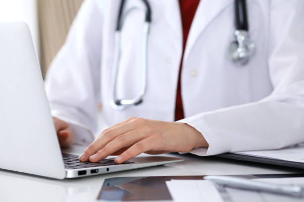 istock Close up of unknown female doctor typing on laptop computer while sitting  at the table 807353684