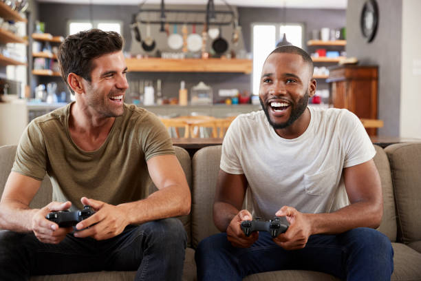 istock Two Male Friends Sitting On Sofa In Lounge Playing Video Game 807384458