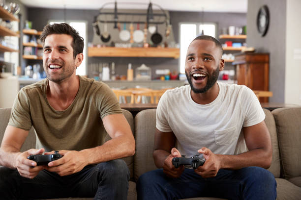 istock Two Male Friends Sitting On Sofa In Lounge Playing Video Game 807384462