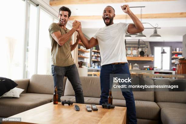 Two Excited Male Friends Celebrate Watching Sports On Television Stock Photo - Download Image Now