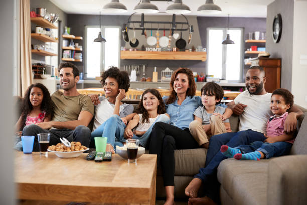 istock Two Families Sitting On Sofa Watching Television Together 807388052
