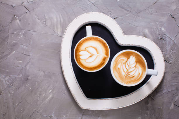 Latte art in two cups of cappuccino on the heart shape tray. Happy morning Valentine day couple