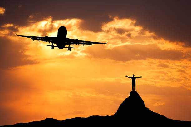 avión y la silueta de un hombre feliz de pie con los brazos levantado para arriba en la cima de la montaña al atardecer. paisaje de verano con aterrizaje avión de pasajeros volando en el cielo naranja con nubes y escalador - leaving business landscape men fotografías e imágenes de stock