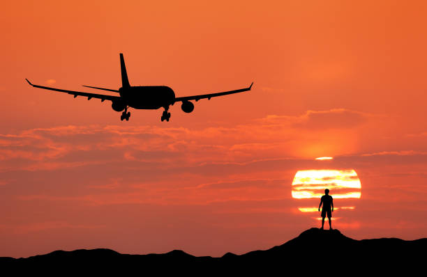 avión y la silueta de un hombre feliz de pie en la colina al atardecer. paisaje de verano con aterrizaje de avión de pasajeros. avión volando en el cielo rojo con nubes, sol y joven hombre deportivo. avión - leaving business landscape men fotografías e imágenes de stock