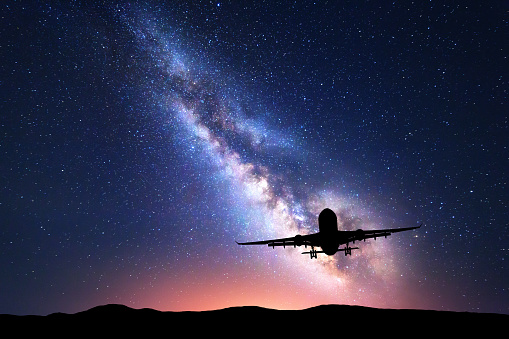 Milky Way and silhouette of a airplane. Landscape with passenger airplane is flying in the starry sky at night. Space background. Commercial airliner on the background of colorful Milky Way. Aircraft