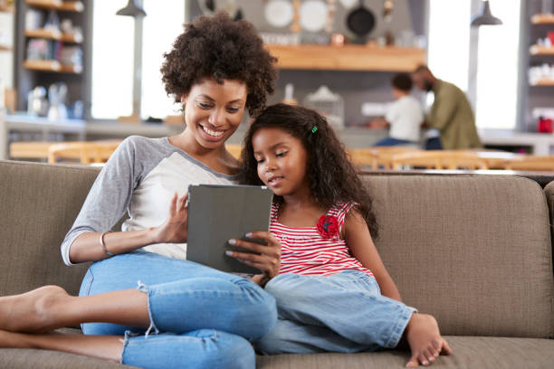 母と娘の上に座るソファのラウンジでデジタル タブレットを使用して - digital tablet family father offspring ストックフォトと画像
