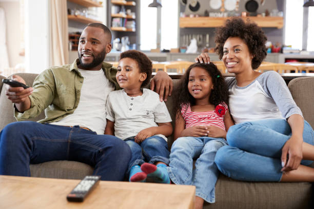 istock Family Sitting On Sofa In Open Plan Lounge Watching Television 807401690