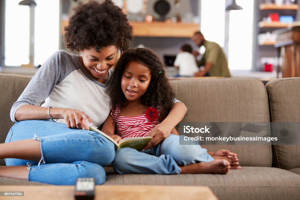 Madre e hija sentarse en el sofá en salón lectura libro juntos - Foto de stock de Niño libre de derechos