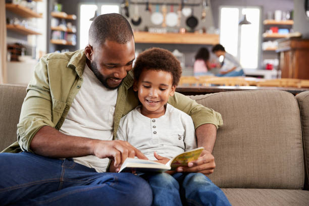 istock Father And Son Sitting On Sofa In Lounge Reading Book Together 807401796