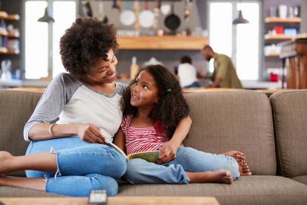 istock Mother And Daughter Sit On Sofa In Lounge Reading Book Together 807401804