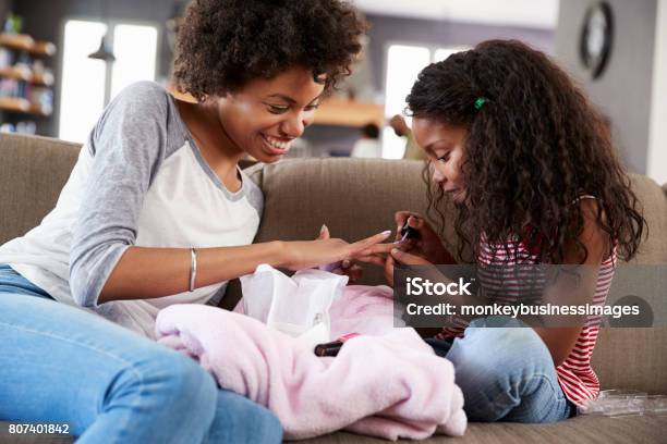 Daughter Sitting On Sofa At Home Painting Mothers Nails Stock Photo - Download Image Now