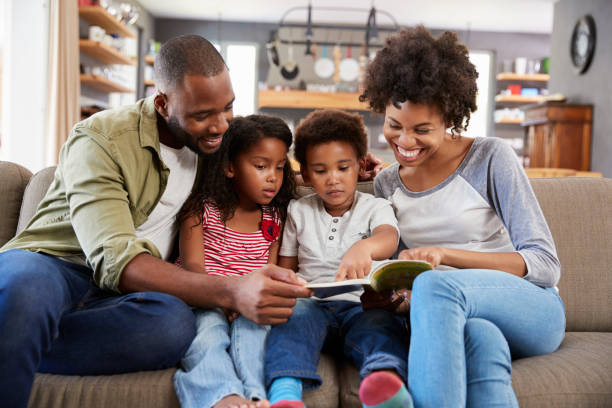 family sitting on sofa in lounge reading book together - family reading african descent book imagens e fotografias de stock