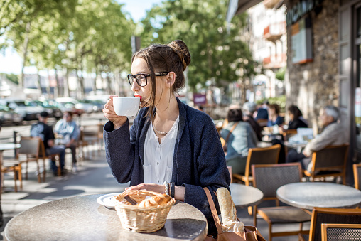 Young woman having a breakfast with coffee and croissant sitting outdoors at the french cafe in Lyon city