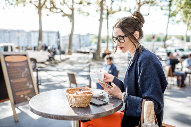 Woman sitting at the cafe outdoors Young woman having a breakfast with coffee and croissant sitting outdoors at the french cafe in Lyon city paris fashion stock pictures, royalty-free photos & images