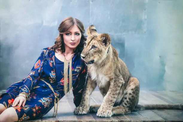 Beautiful fashionable young woman with a cute little alive lion cub