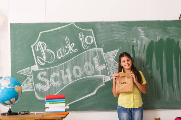 niña adolescente sonriente que se remonta a la escuela - packed lunch lunch paper bag blackboard fotografías e imágenes de stock