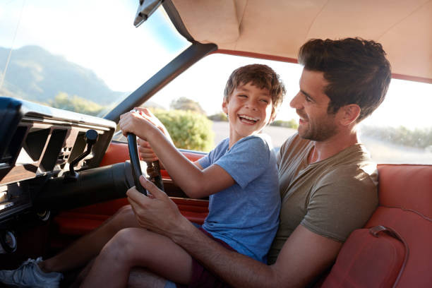 Father Teaching Young Son To Drive Car On Road Trip