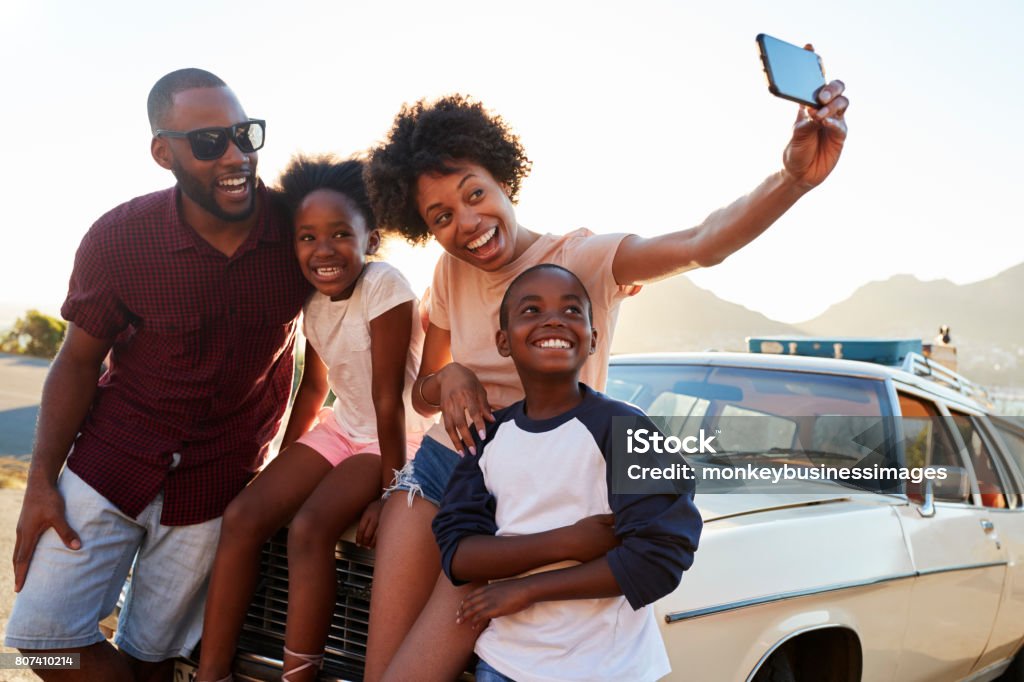 Family Posing For Selfie Next To Car Packed For Road Trip Family Stock Photo