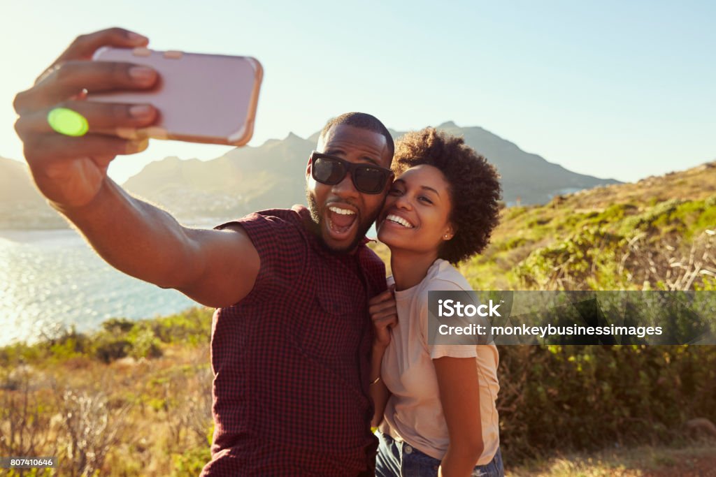 Young Couple Pose For Holiday Selfie On Clifftop Selfie Stock Photo