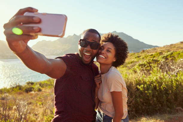 young couple pose for holiday selfie on clifftop - couple black imagens e fotografias de stock
