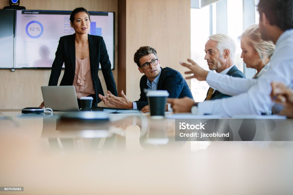 Diverse business group having a meeting in boardroom Team of business people sitting together in discussion around conference table. Diverse business group having a meeting in boardroom. Presentation - Speech Stock Photo