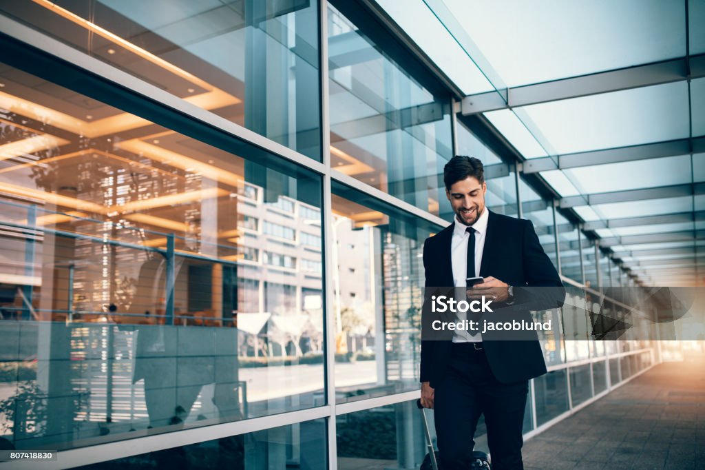 Jeune homme d’affaires marchant avec téléphone mobile à l’aéroport - Photo de Homme d'affaires libre de droits