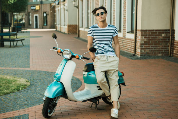 Handsome young man in sunglasses leaning at scooter and looking at camera