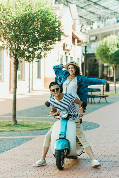 istock Happy stylish young couple riding scooter  and smiling at camera 807419636