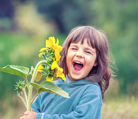 Happy laughing little girl with a sunflower outdoors