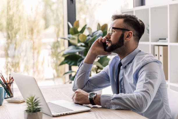 istock handsome bearded businessman using laptop and smartphone in modern office 807434600