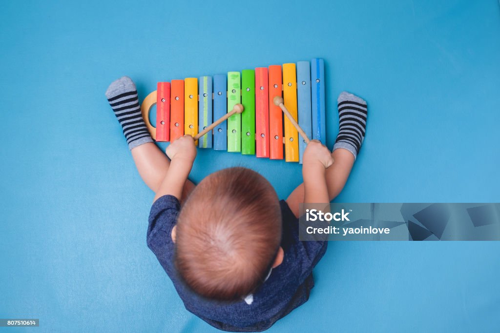 Bird eye view of Cute little Asian 18 months / 1 year old baby boy child hold sticks & plays a musical instrument colorful wooden toy xylophone Bird eye view of Cute little Asian 18 months / 1 year old baby boy child hold sticks & plays a musical instrument colorful wooden toy xylophone, Educational toy for kids and toddlers concept Music Stock Photo