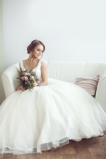 Portrait of a bride with a bouquet in a bright room on a white sofa