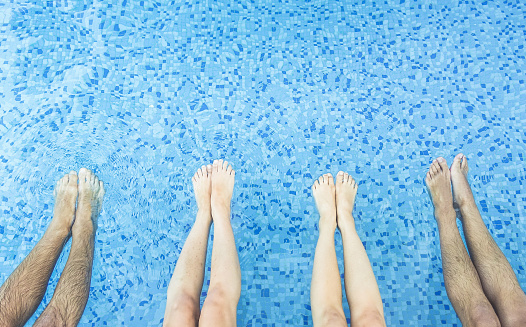 Legs view of friends relaxing and chilling in swimming pool - Young people having fun together outside in hotel resort on summer vacation - Youthand friendship concept - Main focus on center feet