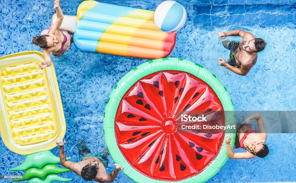 Happy friends playing with ball inside swimming pool - Young people having fun on summer holidays vacation - Travel,holidays,youth,friendship and tropical concept - Seasonal color tones filter Swimming Pool Stock Photo