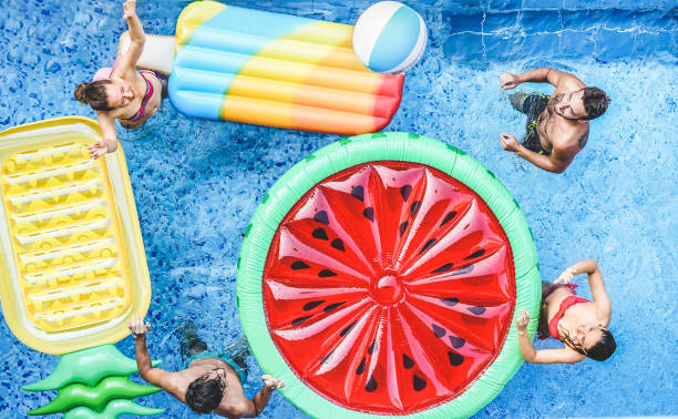 szczęśliwi przyjaciele bawiący się piłką w basenie - młodzi ludzie bawiący się na wakacjach - podróże, wakacje, młodzież, przyjaźń i tropikalna koncepcja - sezonowy filtr kolorów - floating on water women swimming pool water zdjęcia i obrazy z banku zdjęć